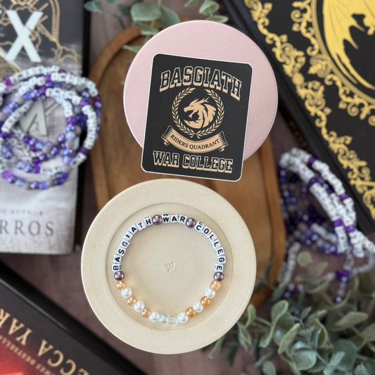 Bracelet with 'BASGLATH WAR COLLEGE' branding on a pink stand, surrounded by decorative items.