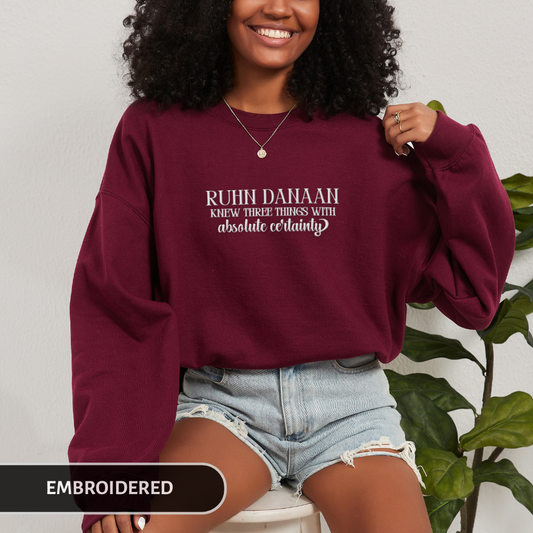 Person wearing a maroon sweatshirt with text, sitting against a neutral background with a plant.