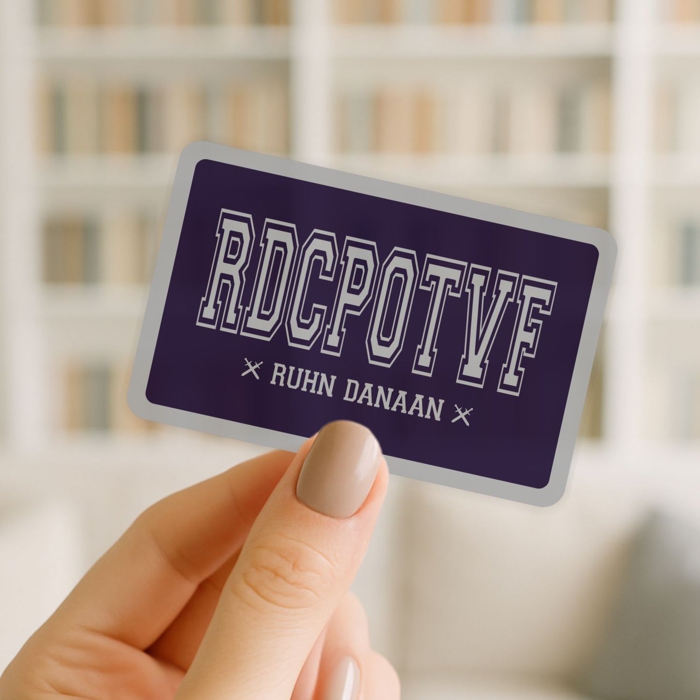 Hand holding a purple card with 'RDCPOTF' and 'RUHN DANAAN' text against a blurred background