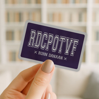 Hand holding a purple card with 'RDCPOTF' and 'RUHN DANAAN' text against a blurred background