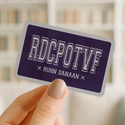 Hand holding a purple card with 'RDCPOTF' and 'RUHN DANAAN' text against a blurred background