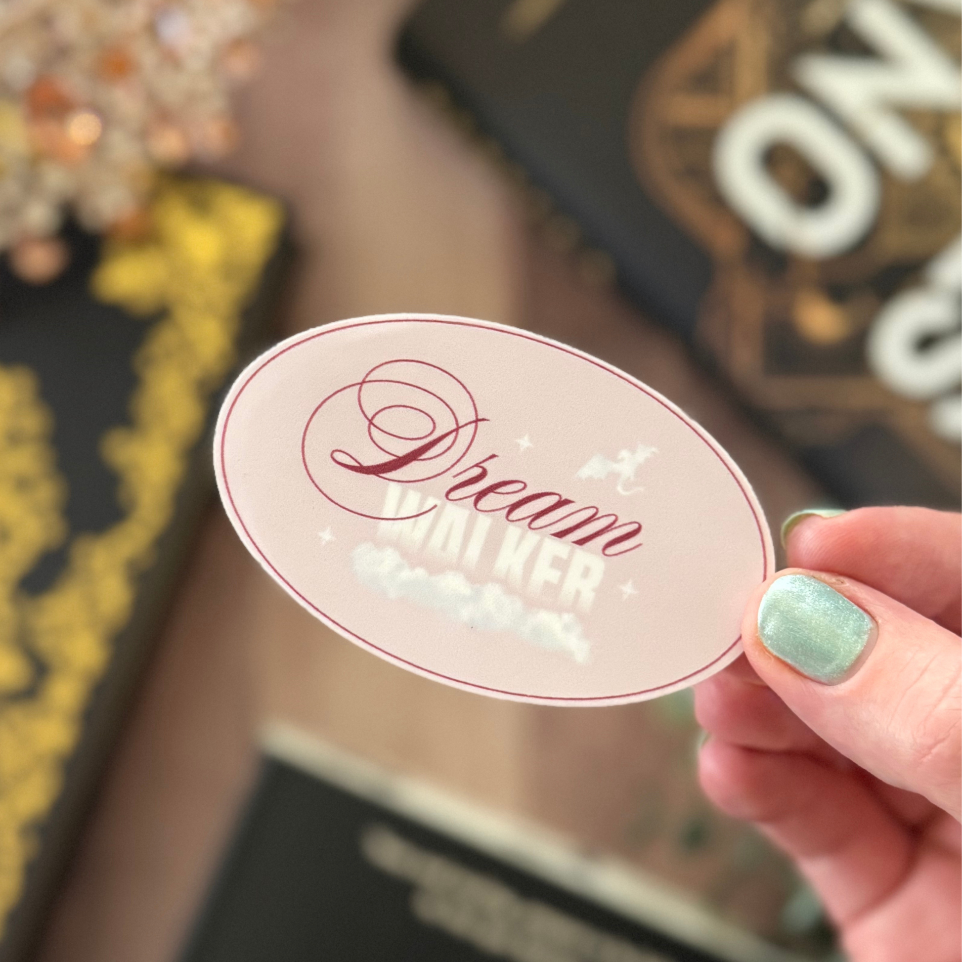 Hand holding a decorative sticker with 'Dream Bigger' text against a blurred background