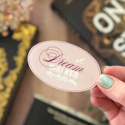 Hand holding a decorative sticker with 'Dream Bigger' text against a blurred background