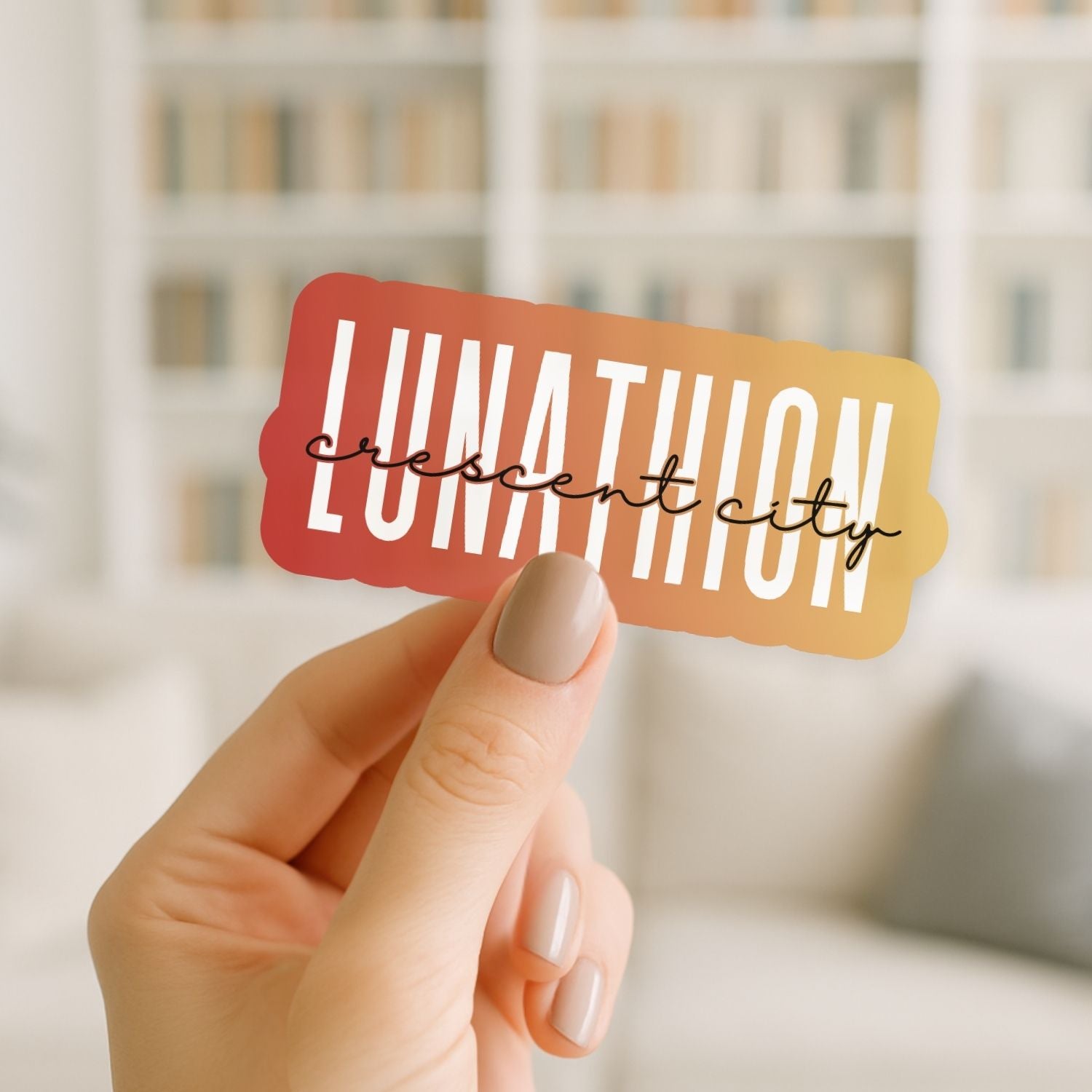 Hand holding a colorful sticker with 'LUNATHION crescent city' text against a blurred indoor background