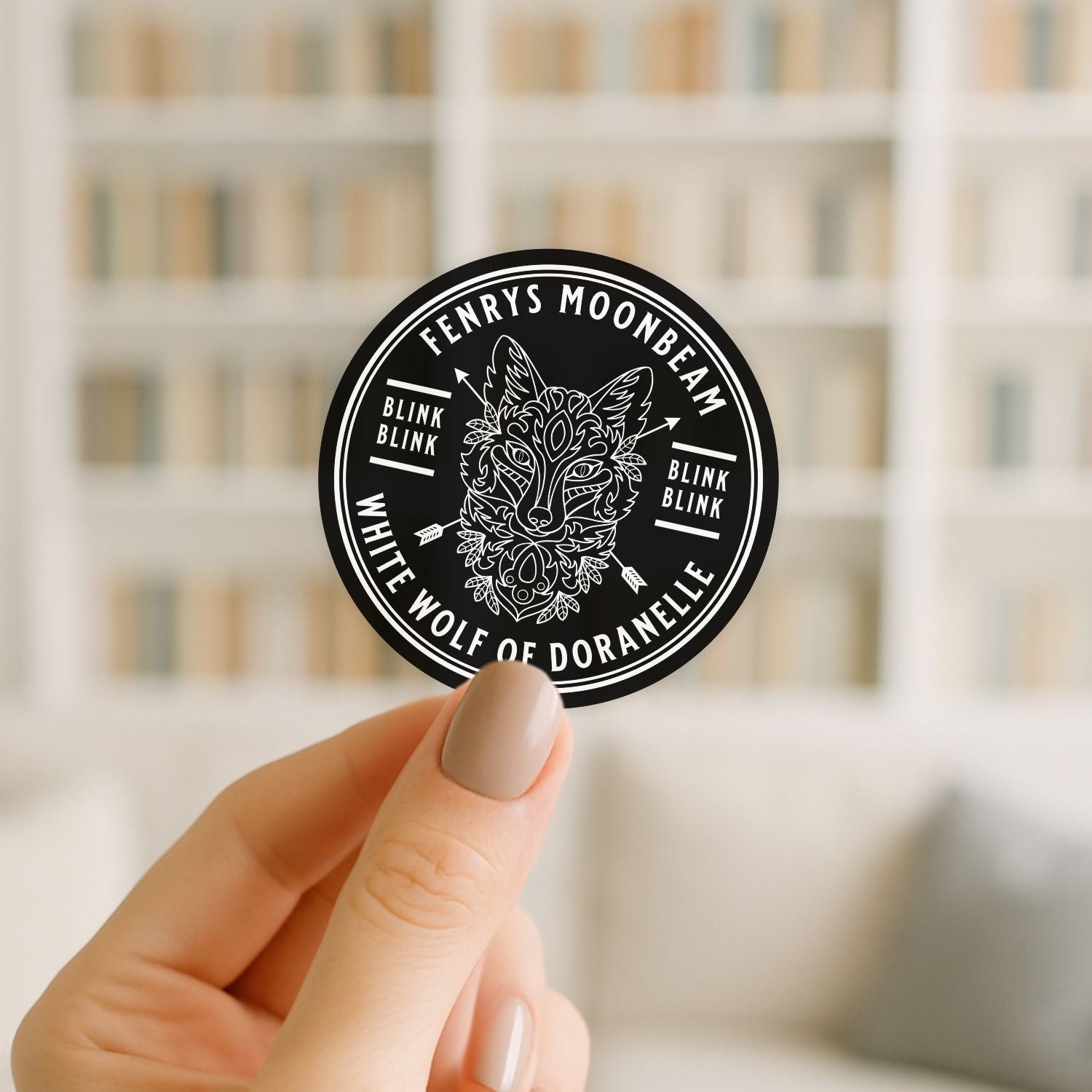 Hand holding a black and white sticker with a wolf design and text against a blurred indoor background.
