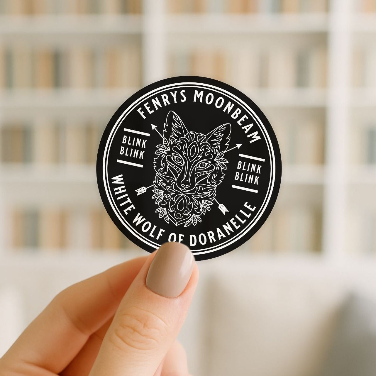 Round black and white sticker with a wolf design held by a hand against a blurred background