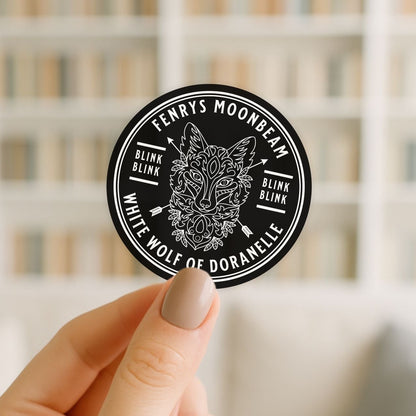 Round black and white sticker with a wolf design held by a hand against a blurred background
