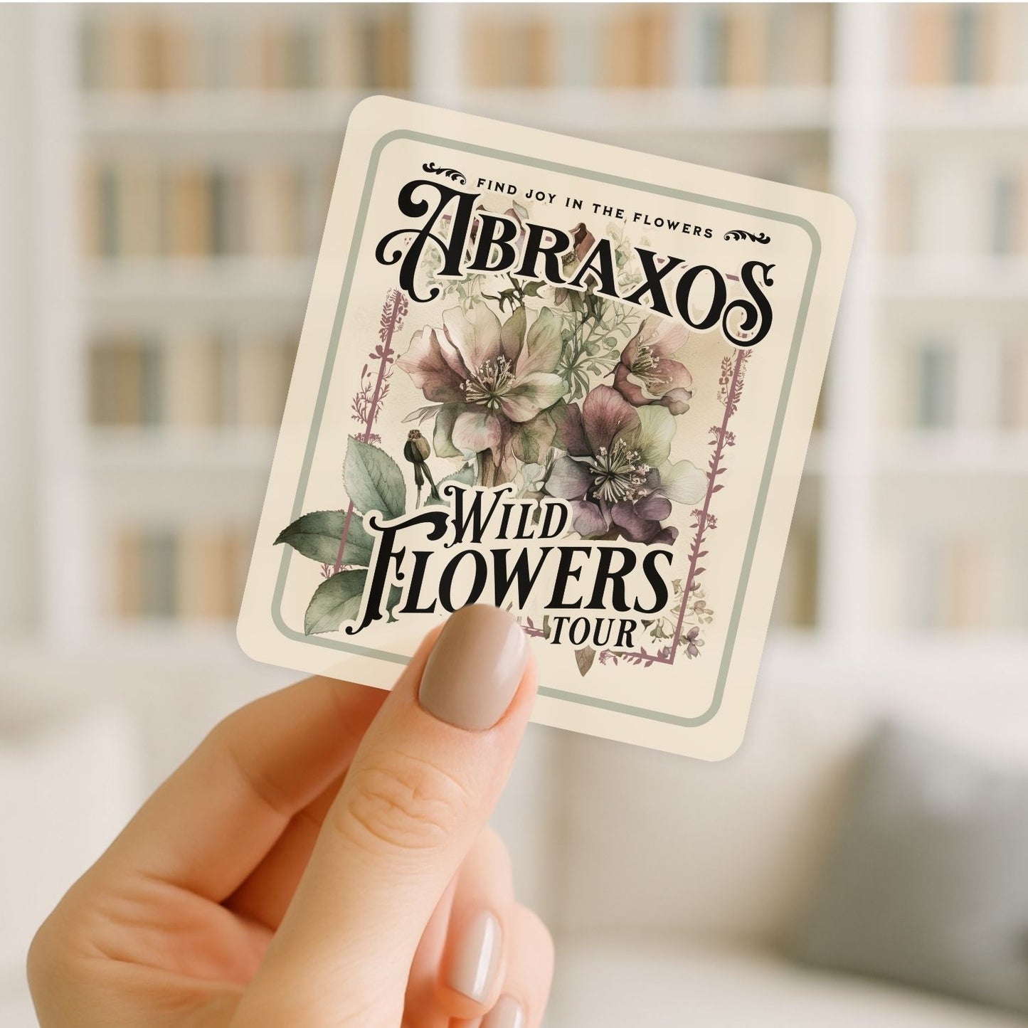 Hand holding a card with 'Abraxos Wild Flowers Tour' design against a blurred background