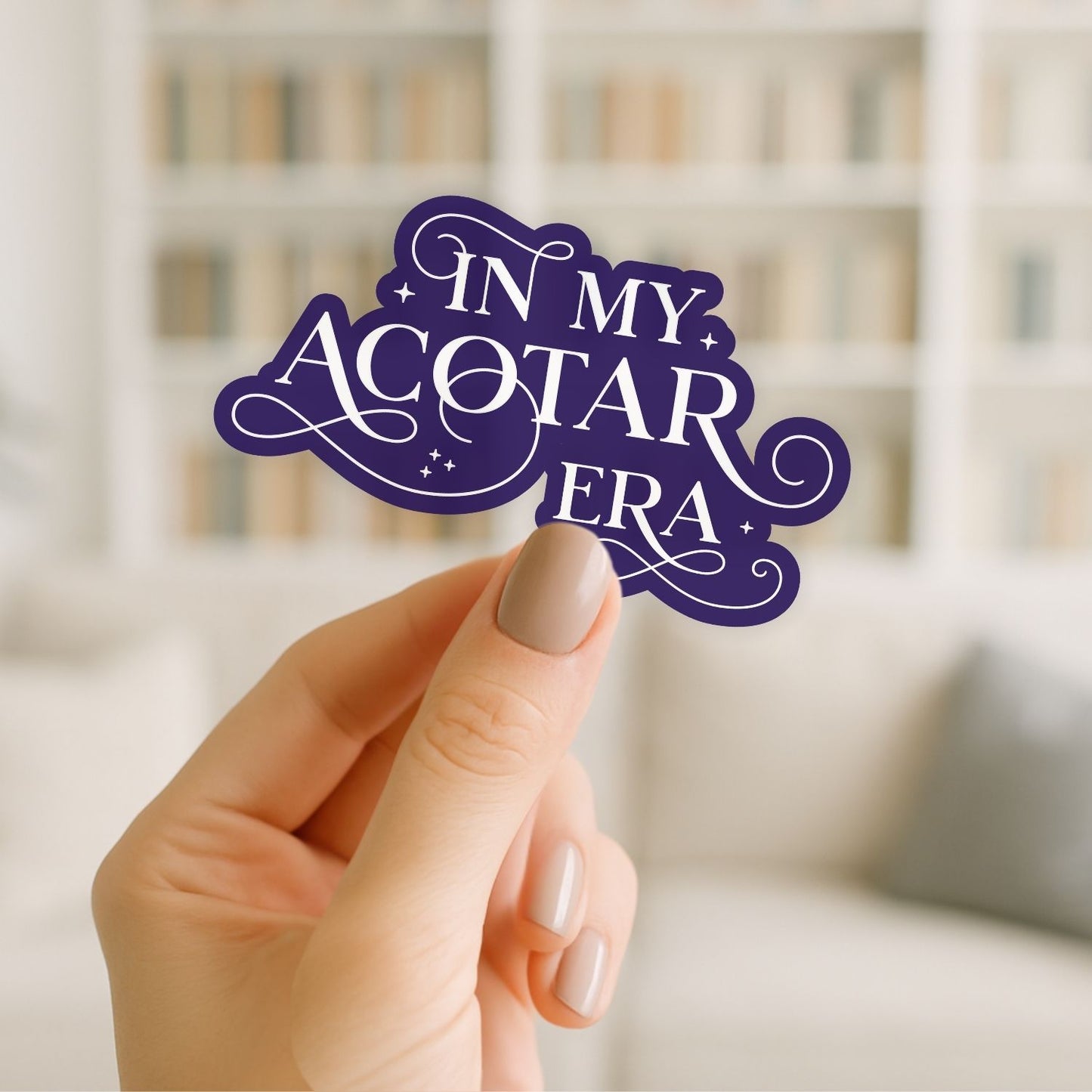 Hand holding a purple 'In my Acotar Era' sign with a blurred bookshelf background