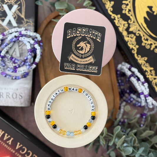 Bracelet with 'BASGLATH WAR COLLEGE' text on a decorative stand with a card in the background.