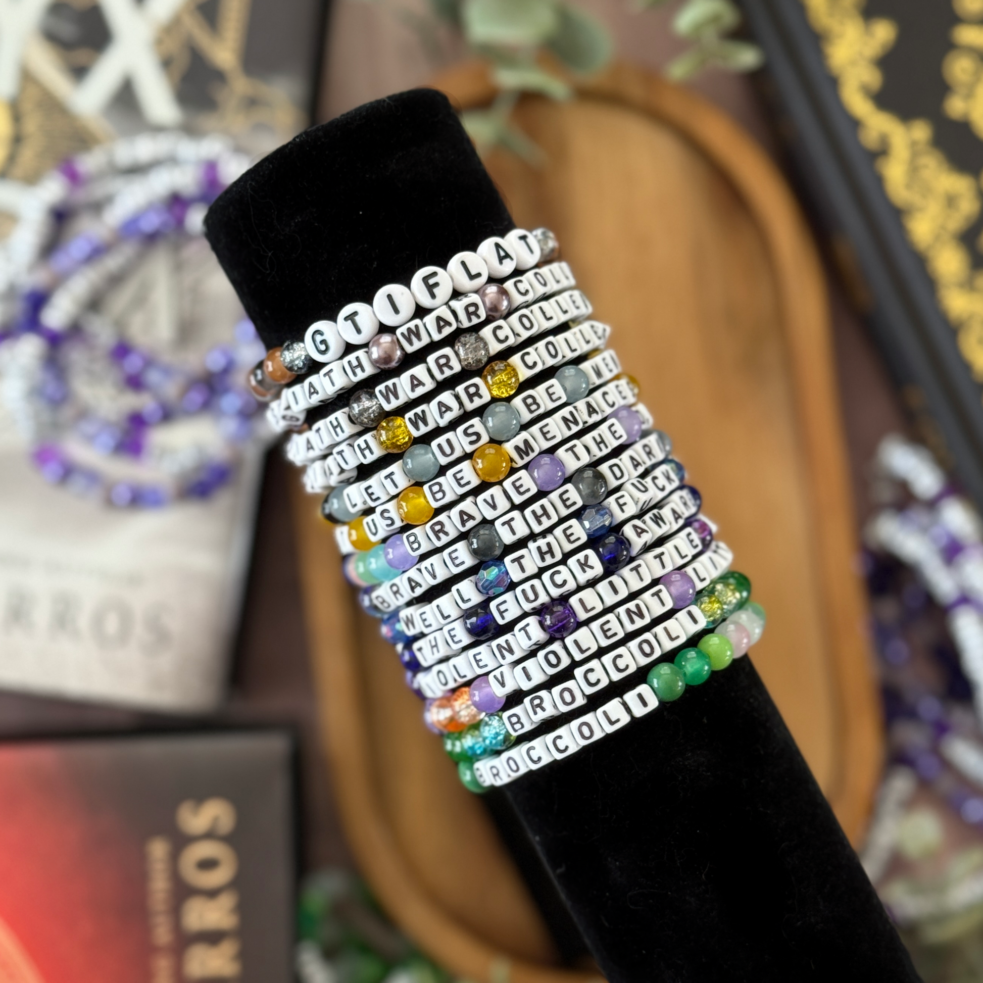 Multicolored beaded bracelet with text on a black band against a blurred background of books and plants.