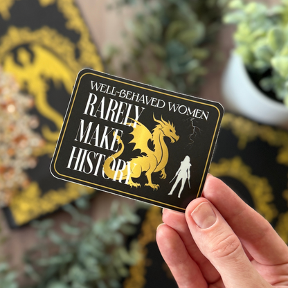 Card with dragon illustration and text held by a hand, with blurred plants in the background