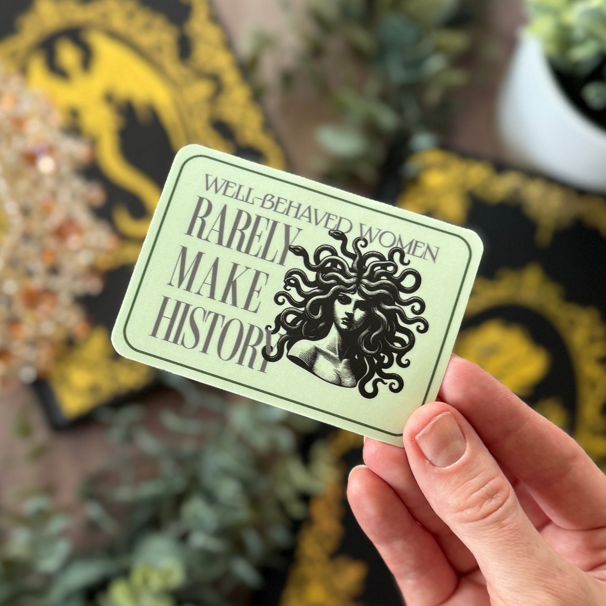 Hand holding a card with text and a graphic of a woman's head, against a decorative background.