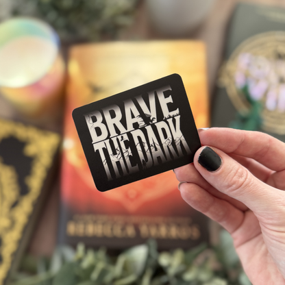 Hand holding a card with 'Brave the Dark' text against a blurred background