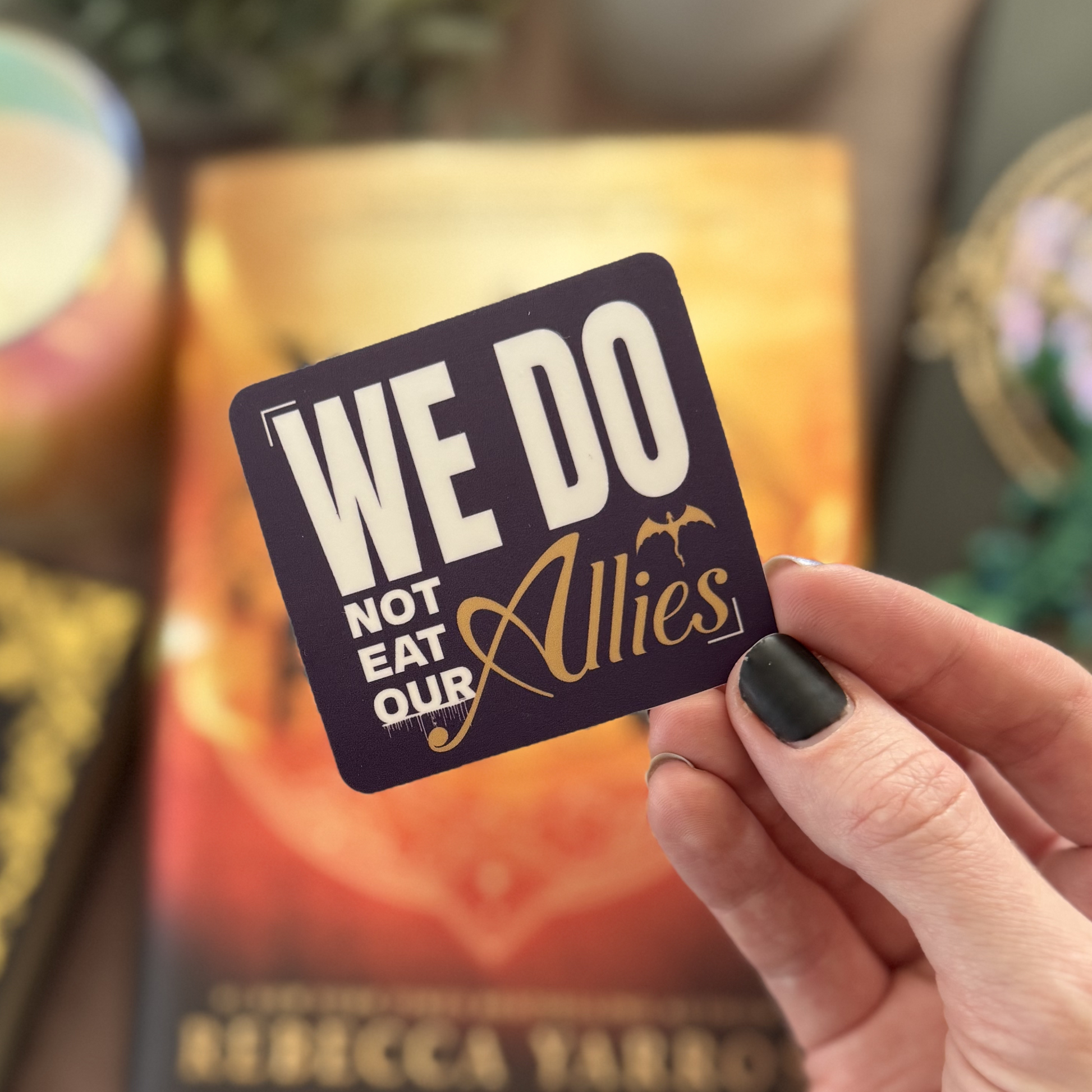 Hand holding a card with 'We Do Not Eat Our Allies' text against a blurred background