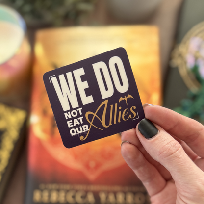 Hand holding a card with 'We Do Not Eat Our Allies' text against a blurred background