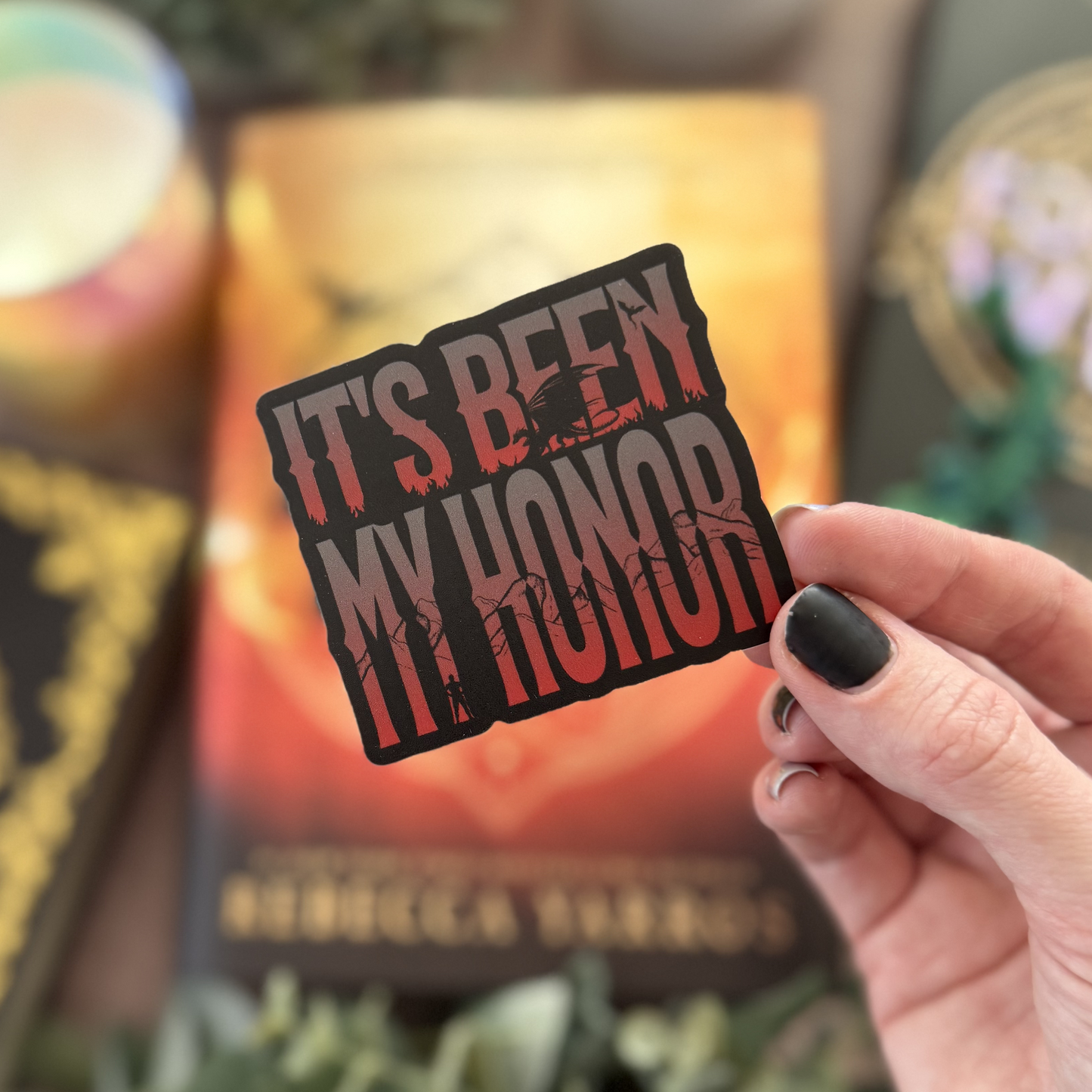 Hand holding a 'It's Been My Honor' sticker with a blurred book in the background