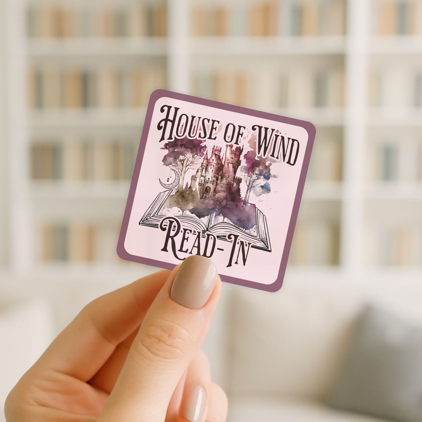 Hand holding a 'House of Wind Read-In' card with a blurred bookshelf background