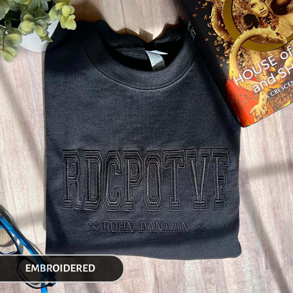 Black embroidered sweatshirt with text on a wooden surface