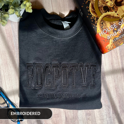 Black embroidered sweatshirt with text on a wooden surface