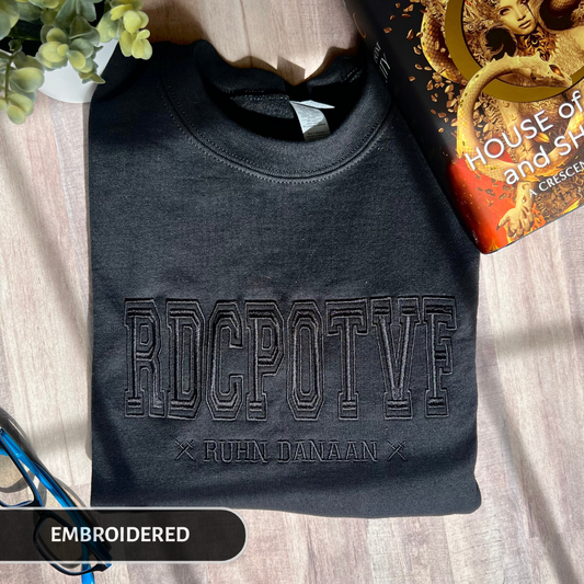 Black embroidered sweatshirt with text on a wooden surface