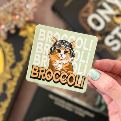 Sticker with a cat illustration and 'BROCCOLI' text held by a hand.