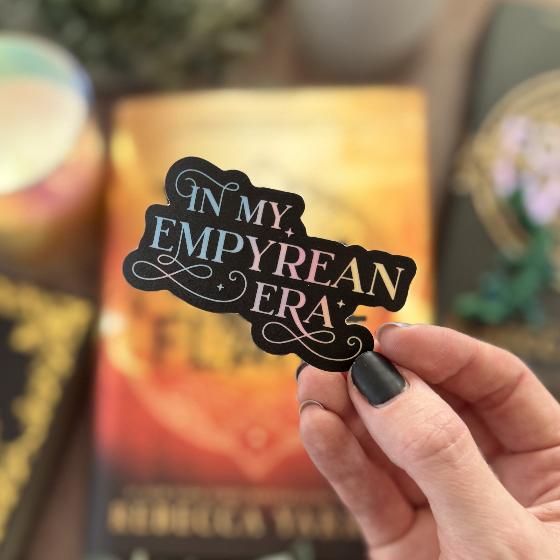 Hand holding a decorative bookplate with 'In My Empyrean Era' text against a blurred book background.