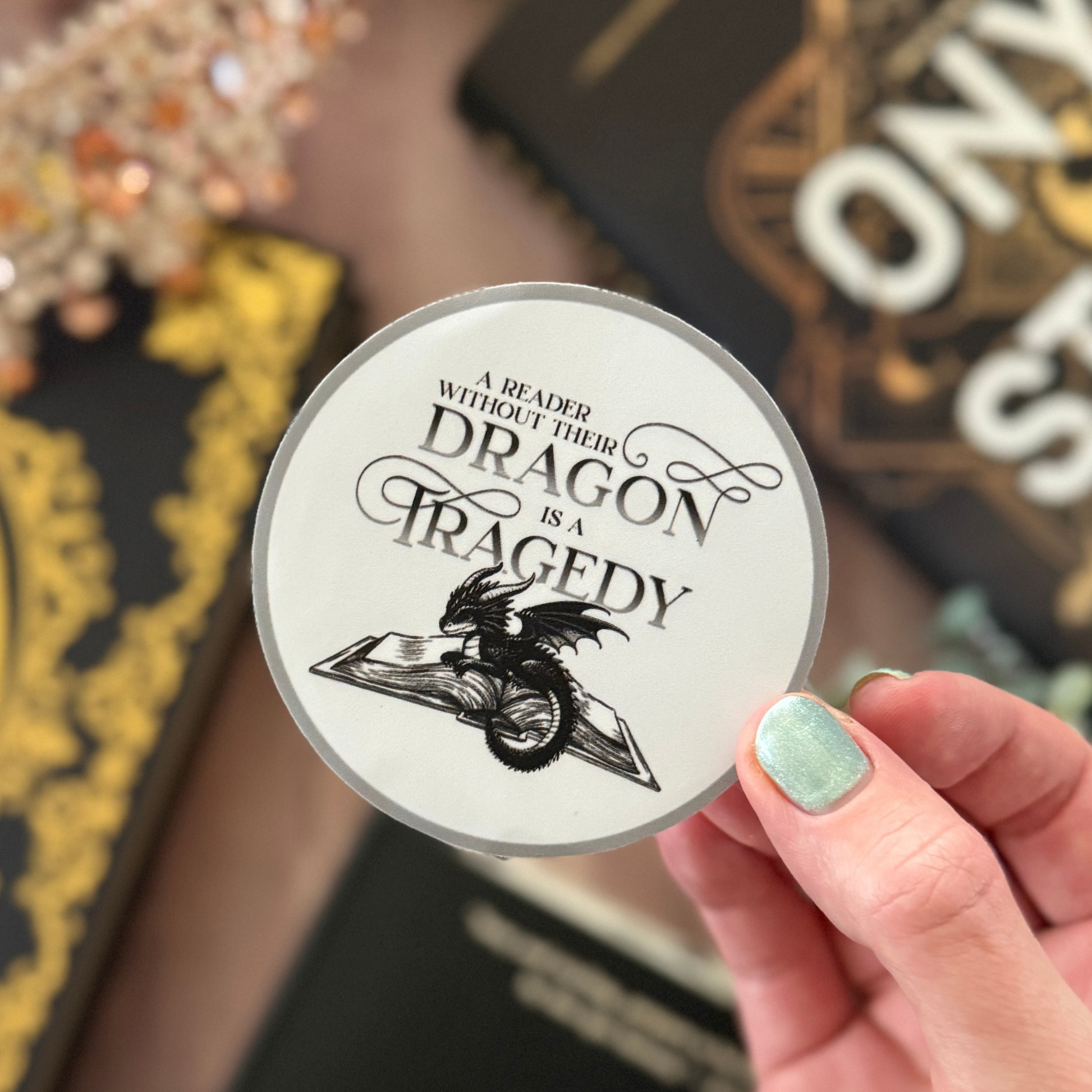 Circular sticker with dragon design and text held by a hand, with books in the background