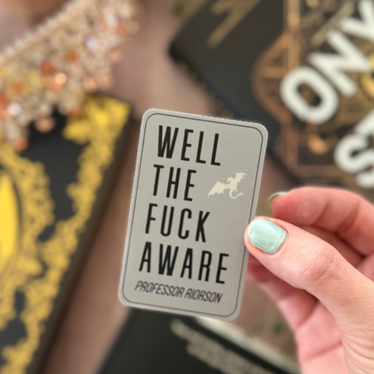 Hand holding a card with text 'WELL THE FUCK AWARE' against a blurred background